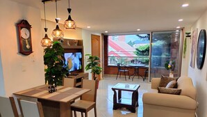 A modern living room with a dining area, a sofa, and a TV. There is a large window with a view of buildings and trees. - Exclusive, luxurious, centrally located apartment — serene and comfortable 302 (Medellín)