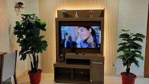 A modern living room with a flat-screen TV mounted on a wooden entertainment unit, flanked by potted plants. - Exclusive, luxurious, centrally located apartment — serene and comfortable 302 (Medellín)
