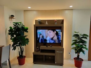 A modern living room with a flat-screen TV mounted on a wooden entertainment unit, flanked by potted plants. - Exclusive, luxurious, centrally located apartment — serene and comfortable 302 (Medellín)