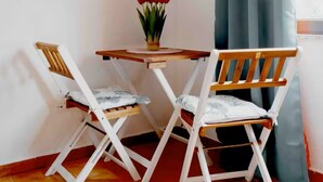 Een hoekzaal met een klein tafeltje en twee stoelen, een vaas met bloemen en een raam met gordijnen.