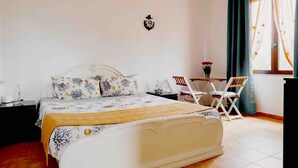 Een netjes opgemaakte slaapkamer met een bed, nachtkastje, stoel en een klein tafeltje met een bloevas.