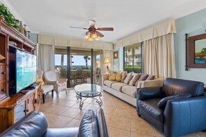 A spacious living room with a television, leather sofas, a glass coffee table, and a ceiling fan. - Bluewater 106 | Beach Front (Orange Beach)