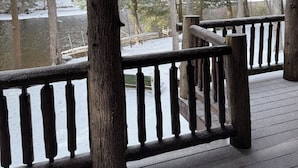 Una terraza de madera con barandilla que da a un paisaje nevado y un cuerpo de agua.