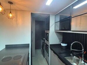 Cozinha moderna com micro-ondas, forno e pia. Possui duas luminárias pendentes e um armário acima da pia.