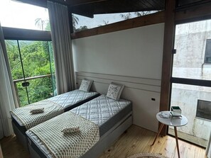 Quarto com duas camas, uma mesinha e vista para o verde lá fora.