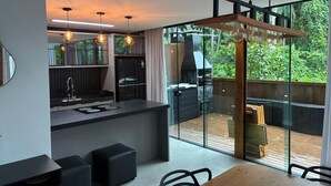 Une cuisine moderne dotée d’un îlot central, d’un coin repas avec une table en bois et d’une porte-fenêtre coulissante donnant sur une terrasse avec un barbecue.