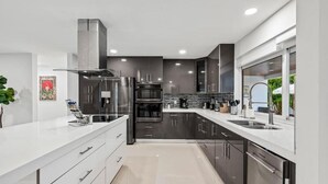 A modern kitchen with stainless steel appliances, a white countertop, and dark cabinetry. - Villa Bonita Tropical Paradise Pool (Hollywood)
