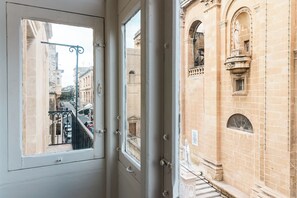 A view through a window of a building with a balcony, a street, and a statue. - Florette Suites (Floriana)
