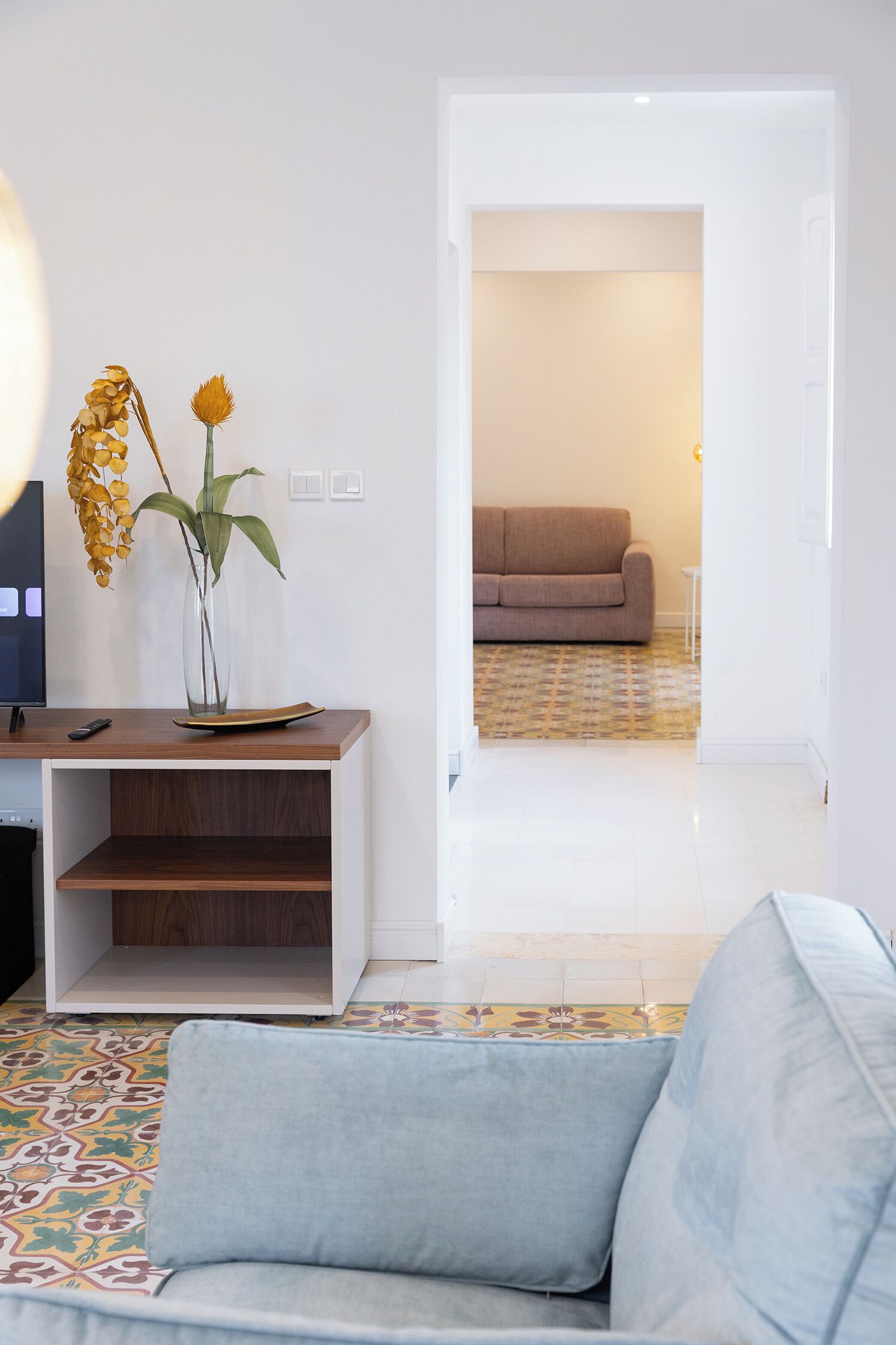 A living room with a sofa, a coffee table, a TV, and a vase with flowers.