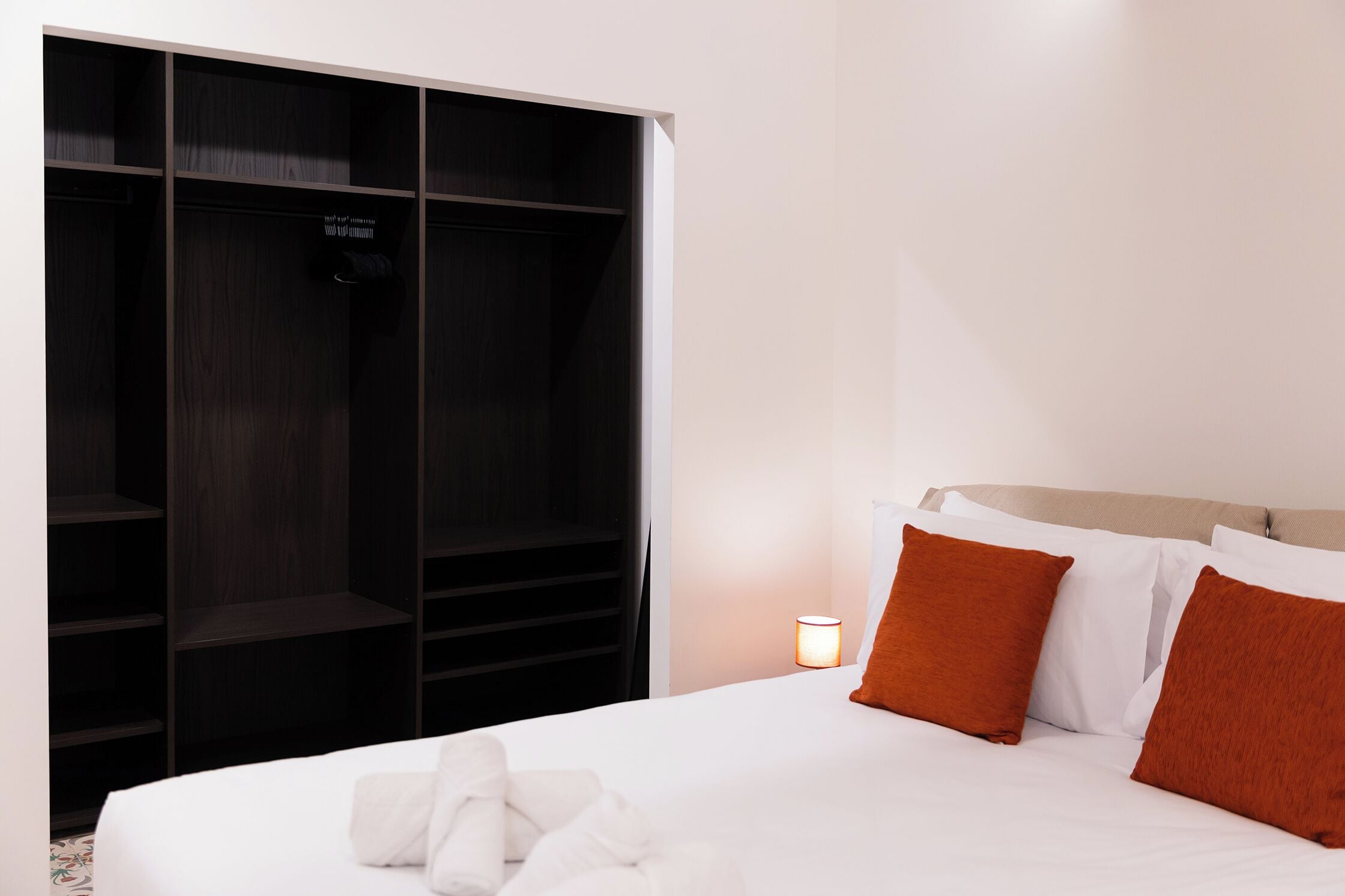Une chambre d’hôtel avec un lit, des oreillers blancs, un oreiller marron, une lampe de chevet et une armoire.