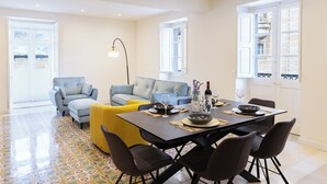 A dining area with a table set for four, a sofa, and a yellow ottoman. - Florette Suites (Floriana)