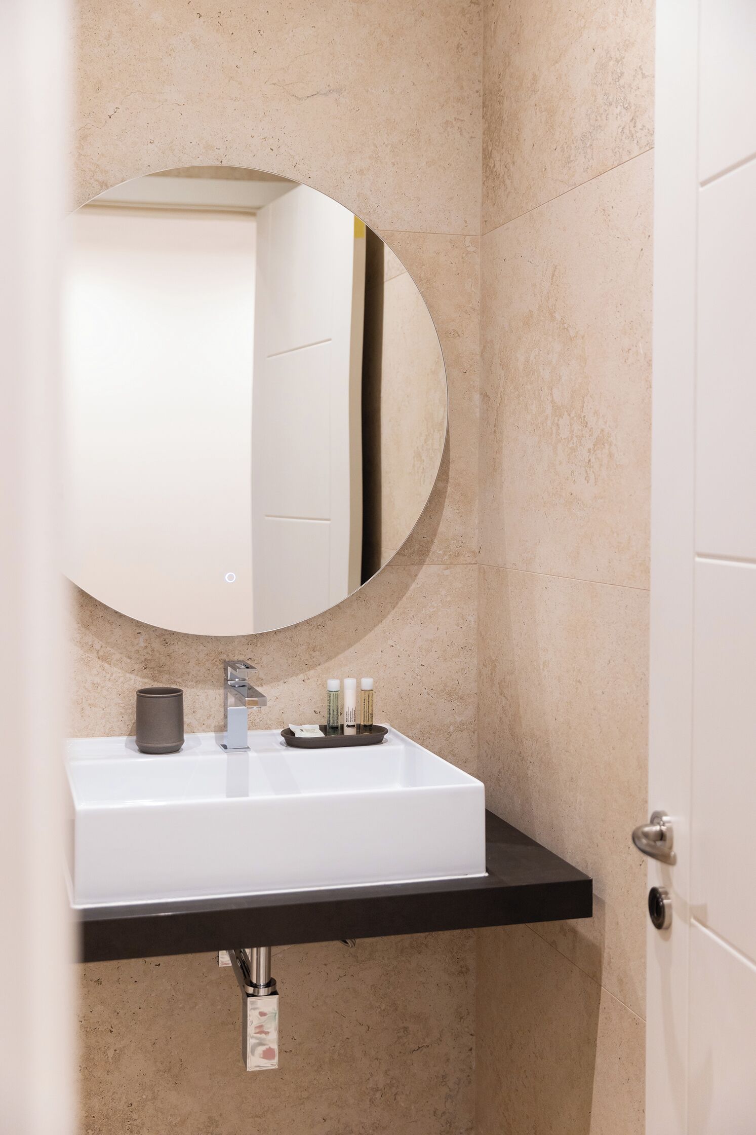 Un baño con un lavamanos blanco, un espejo redondo y una encimera negra.