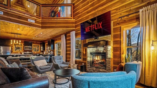 Interior acogedor de una cabaña de troncos con chimenea, un letrero de Netflix y una cocina moderna.