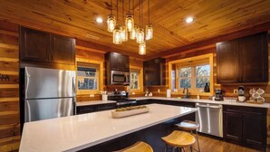 Una cocina moderna con una isla grande, electrodomésticos de acero inoxidable, gabinetes de madera oscura y una lámpara colgante.