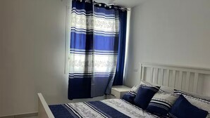 Un dormitorio con cama, mesita de noche y cortinas.
