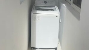Una lavadora compacta y blanca de carga frontal en un pasillo estrecho con una ventana en un lateral.