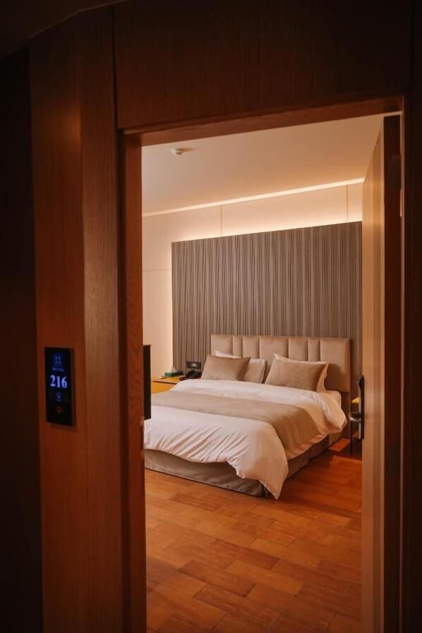 A hotel room with a bed, wooden flooring, a headboard, and a digital display showing room number 216. - Hotel ehden (Ehden)