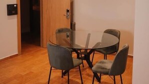 A modern dining area with a glass table and four chairs, wooden flooring, and a wooden door.