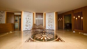 A modern hotel lobby with a central seating area, a decorative floor pattern, and a sign reading "HOTEL EHDEN".