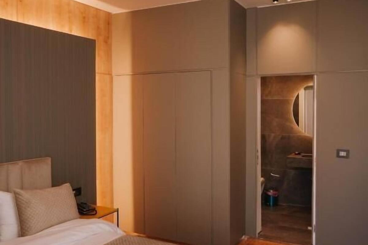 A modern hotel room with a large bed, a wardrobe, and a bathroom visible through an open door.
