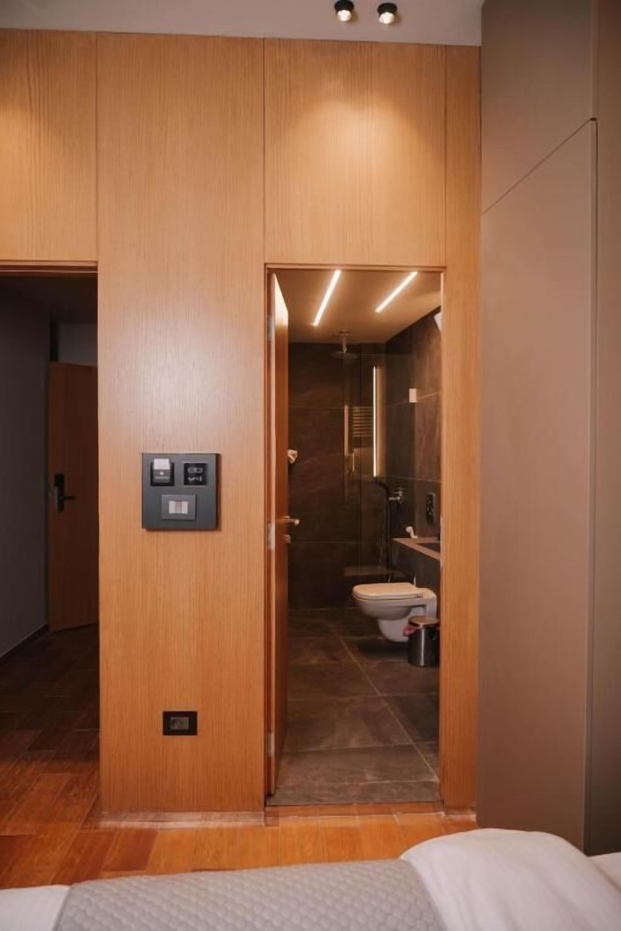 A hotel room with a wooden wardrobe, a bed, and a bathroom with a shower and toilet.