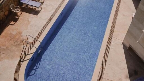 A rectangular swimming pool with a blue interior, surrounded by lounge chairs and a sunshade.