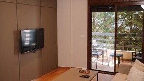 A modern living room with a flat-screen TV mounted on the wall, a sofa, a coffee table, and a sliding glass door leading to an outdoor area with a table and chairs. - Hotel ehden (Ehden)