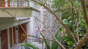 Un hombre y una mujer en un balcón con un muro decorativo y abundante vegetación al fondo.