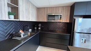 Una cocina moderna con armarios oscuros, un microondas, un refrigerador y un salpicadero con motivo de espiga.