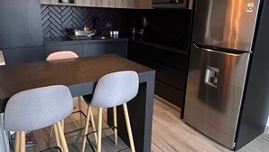 Una cocina moderna con una isla central, dos lámparas colgantes, un refrigerador de acero inoxidable y un salpicadero con motivo de espiga.
