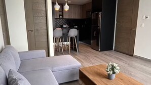 Una sala moderna con un sofá seccional gris, una mesa de centro de madera y una cocina al fondo.