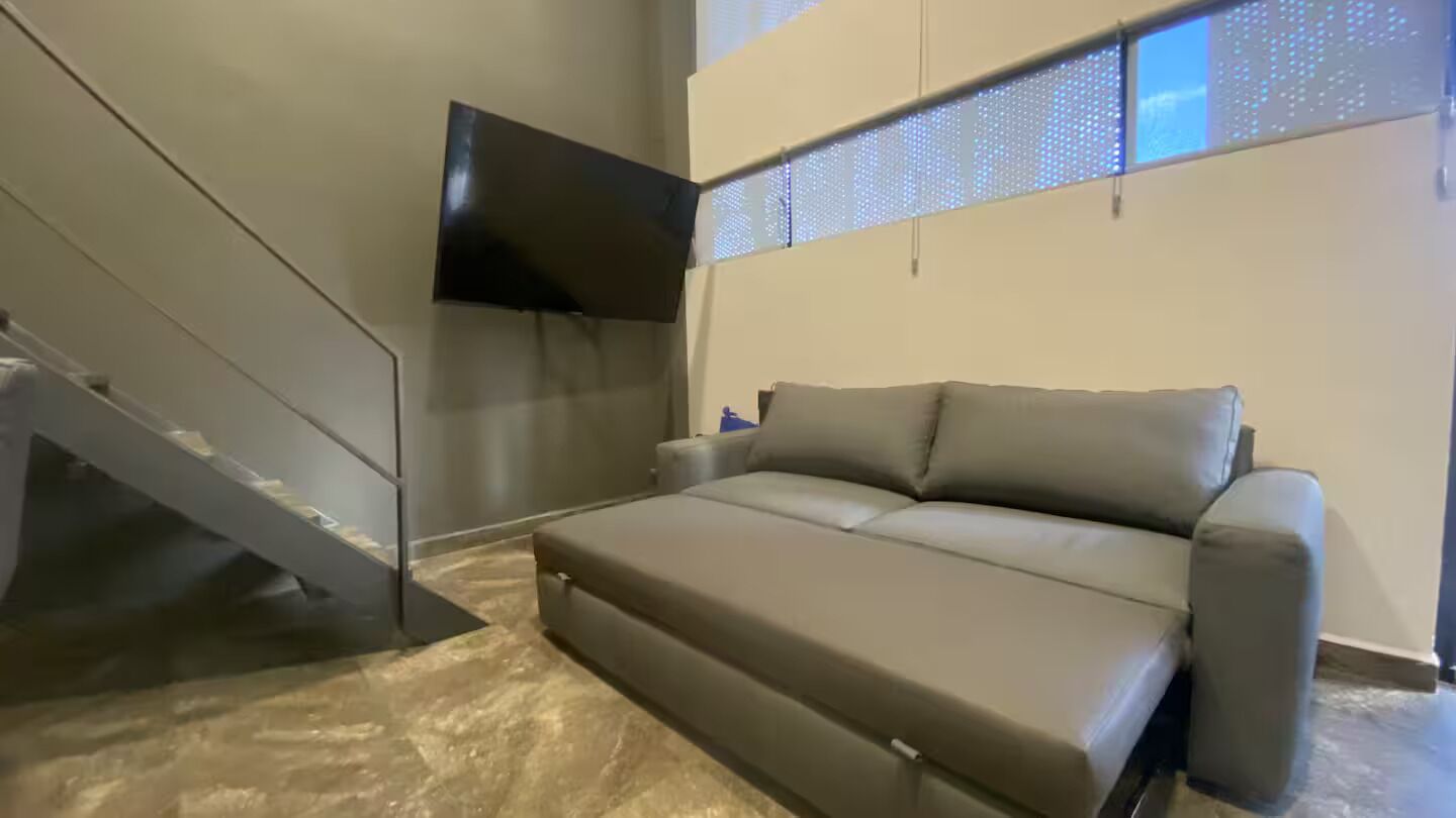 Un salon moderne avec un canapé, un téléviseur à écran plat fixé au mur et un escalier.