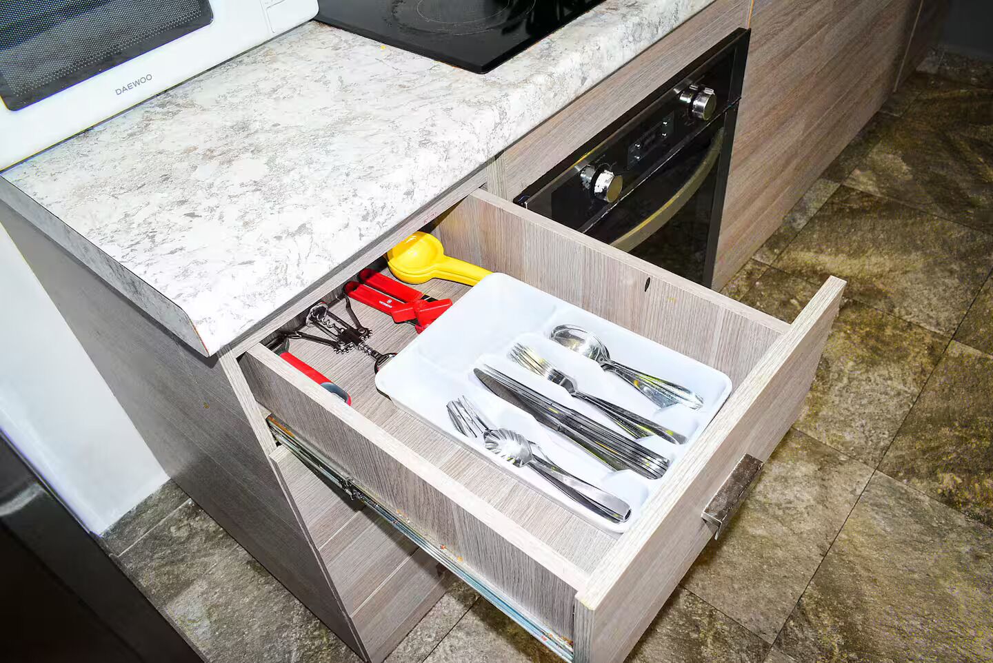 Un tiroir de cuisine contenant des ustensiles et une spatule jaune.
