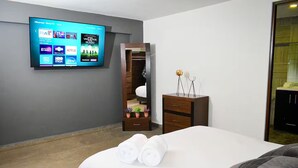 Camera d'albergo con un letto, una TV a muro, un armadio e un tavolino con soprammobili.