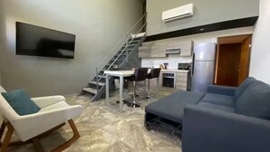 Un soggiorno moderno con un divano grigio, una poltrona bianca e una scala che conduce a una zona cucina.