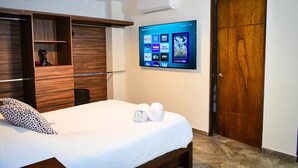 Ein Hotelzimmer mit einem Bett, einem Holzschrank, einem an der Wand befestigten Fernseher, der Streaming-Dienste anzeigt, und einer Tür.