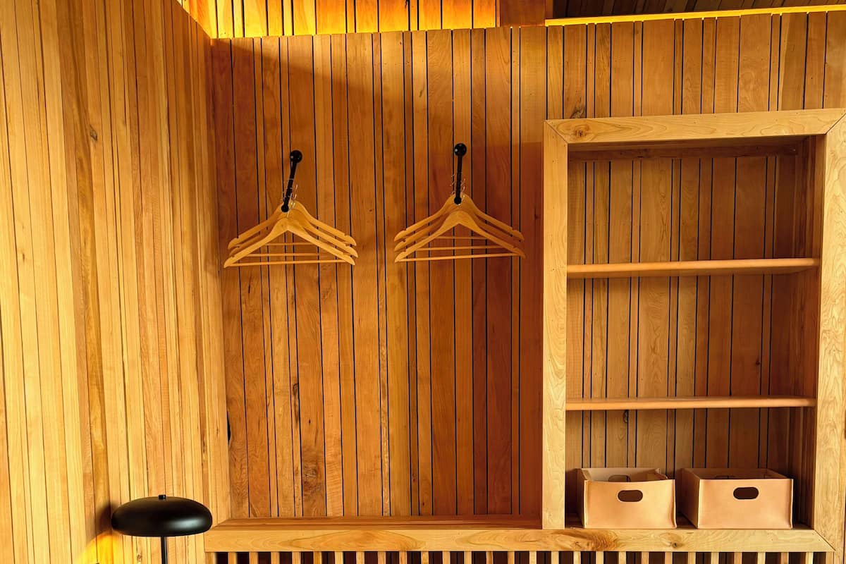 A wooden room with a bed, two wooden hangers, a shelf with storage boxes, and a black floor lamp.
