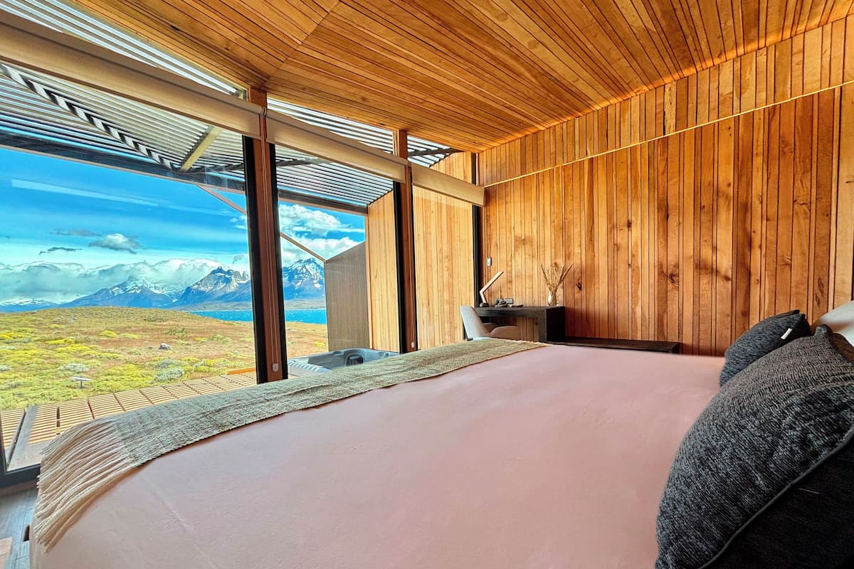 A bedroom with a large bed, wooden walls, and a view of mountains and a lake.