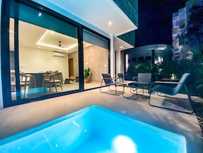 Ein moderner Poolbereich im Freien mit Liegestühlen, einem Essbereich und Blick ins Innere.