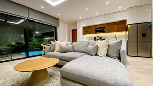 Ein modernes Wohnzimmer mit Ecksofa, Couchtisch aus Holz und einer Küchenzeile mit Schränken und Geräten.