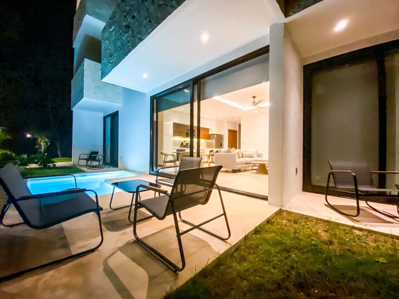A modern house with a swimming pool, outdoor seating, and a glass door leading to a living area.