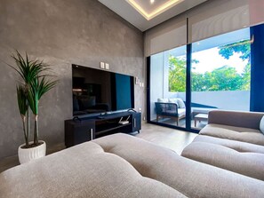 Ein modernes Wohnzimmer mit einem Flachbildfernseher, einer großen Topfpflanze und einem Sofa.