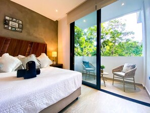 Ein Schlafzimmer mit einem großen Bett, einem Nachttisch, einer Wanduhr und einer Glastür, die zu einem Balkon mit zwei Stühlen im Freien führt.