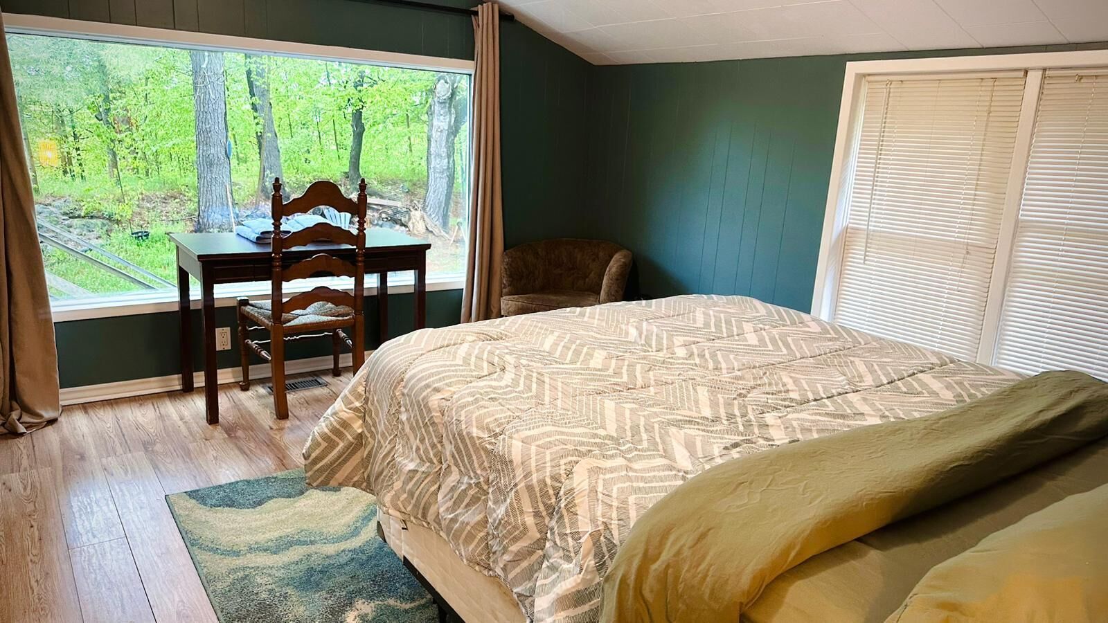 A bedroom with a large window, a bed, a chair, and a small table.