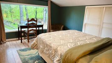 A bedroom with a large window, a bed, a chair, and a small table.