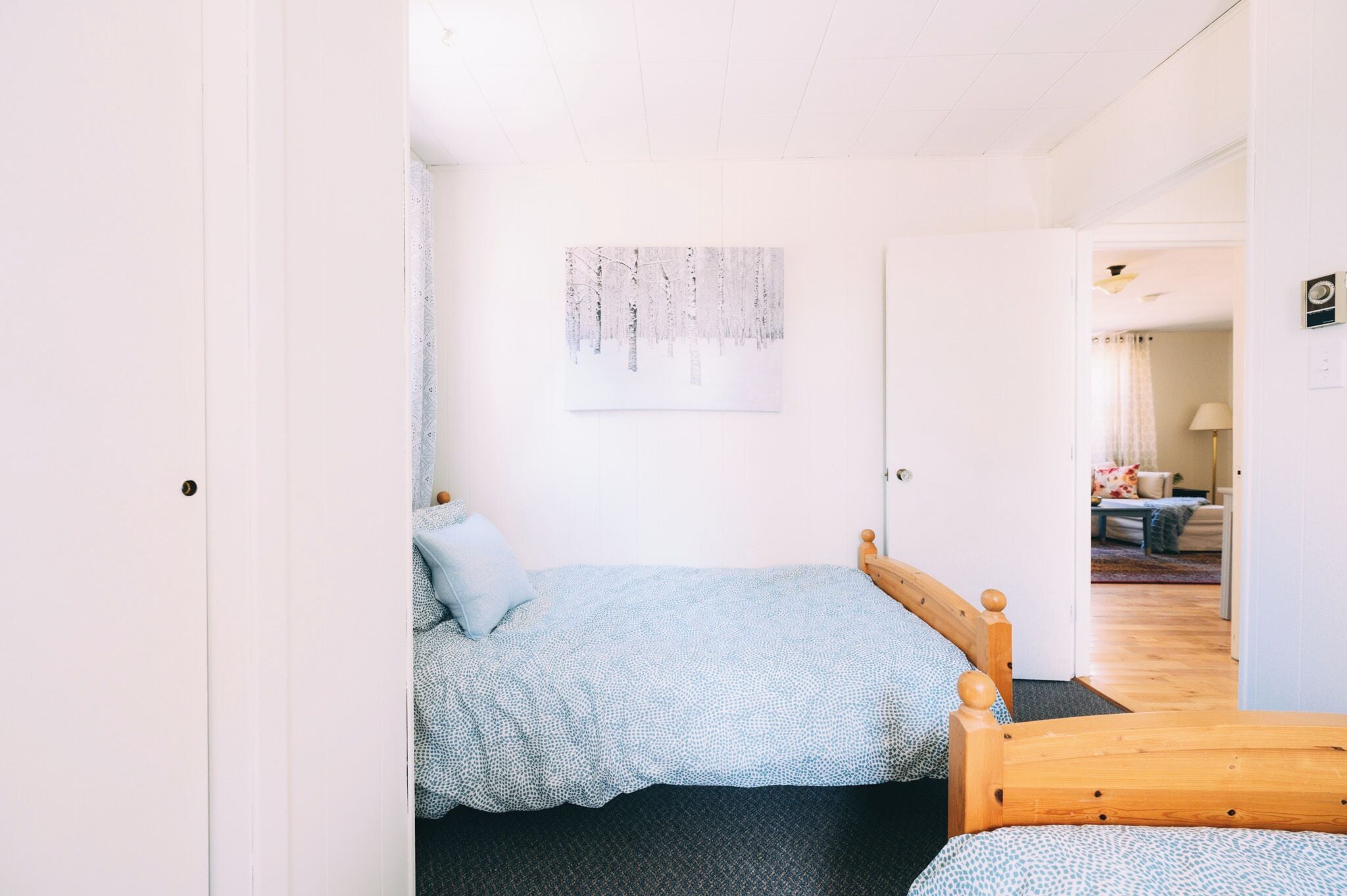 A bedroom with a bed, a wooden headboard, a wall-mounted artwork, and a door leading to another room.