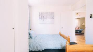 A bedroom with a bed, a wooden headboard, a wall-mounted artwork, and a door leading to another room.