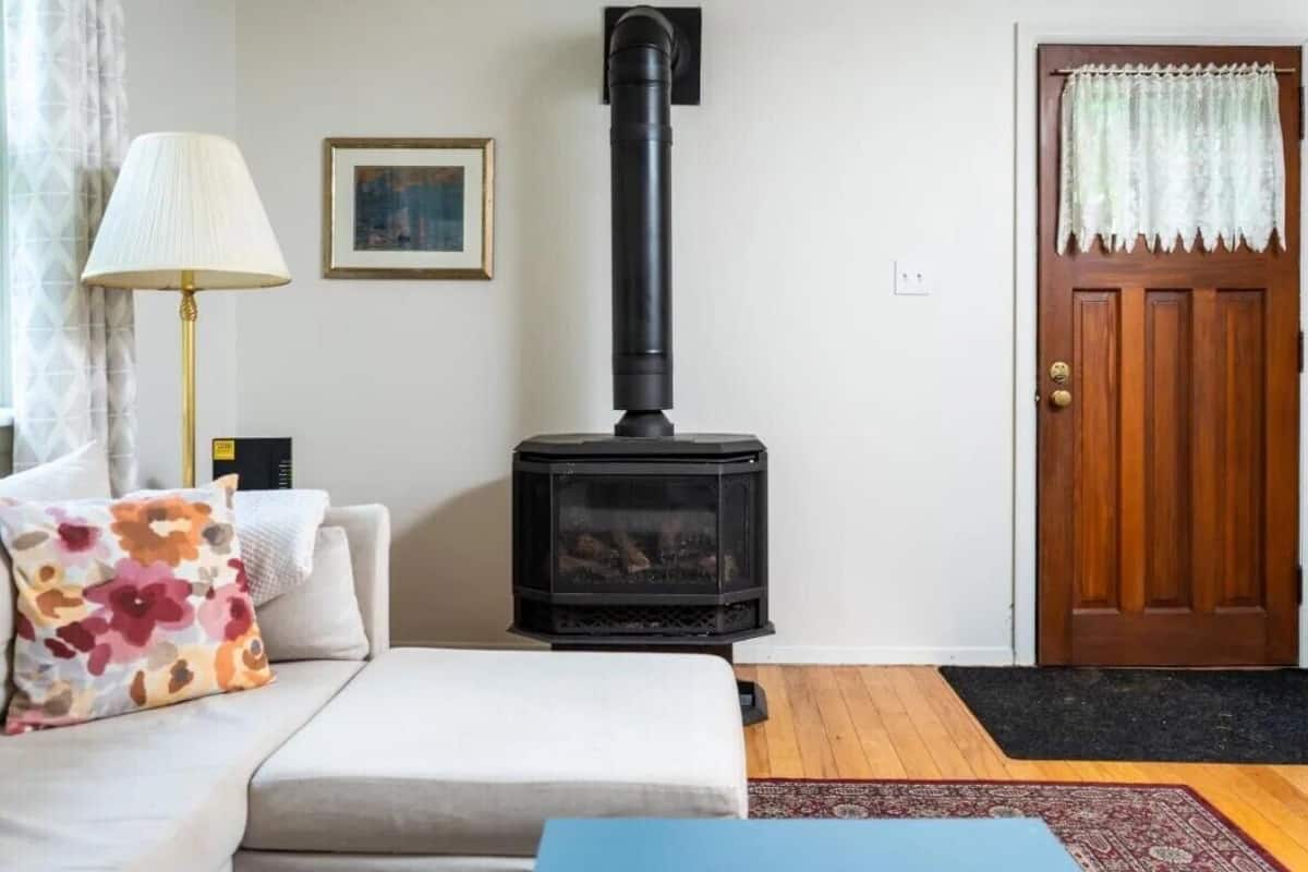 A living room with a sofa, a lamp, a framed picture, a black wood-burning stove, and a wooden door.