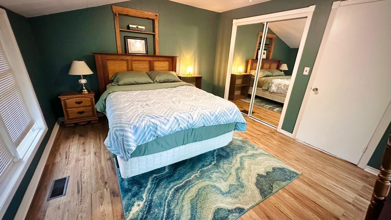 Un dormitorio con una cama, una mesita de noche, una lámpara, un espejo y una puerta.