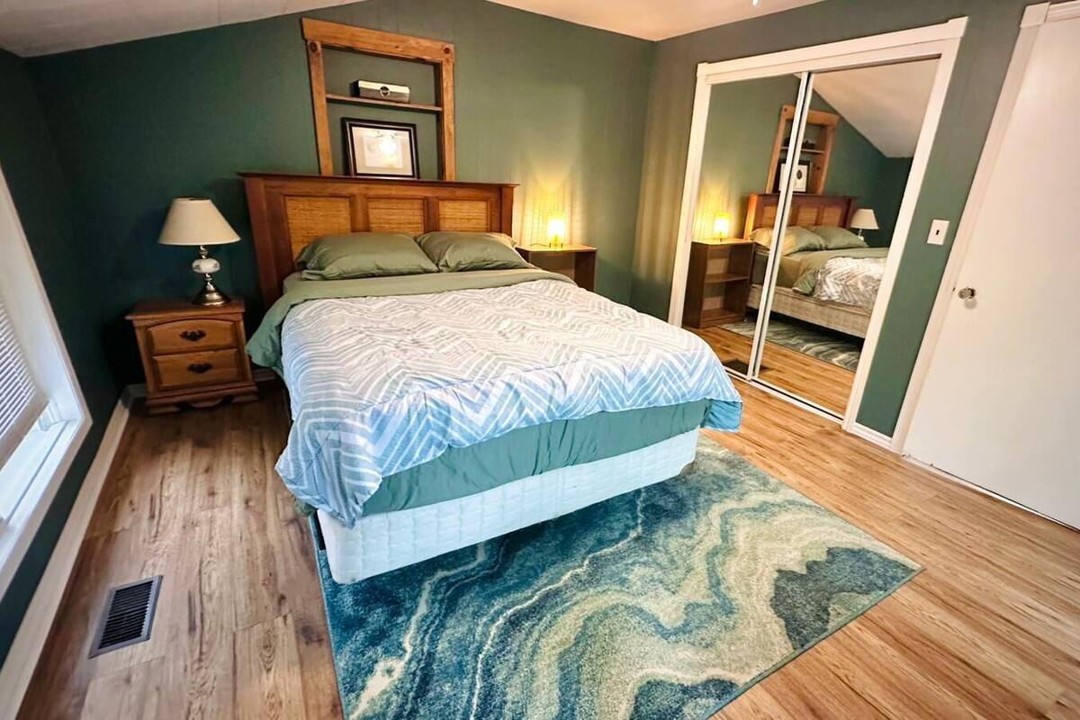 A bedroom with a bed, a nightstand, a lamp, a mirror, and a door.